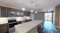This single-floor residence in Wausau, Wisconsin, presents a cohesive modern design highlighted by quality finishes throughout. The kitchen serves as a central focal point, showcasing an expansive granite island illuminated by industrial-style pendant lights. Dark espresso cabinetry with under-cabinet lighting pairs with a full suite of stainless steel appliances, including a refrigerator, range, microwave, and dishwasher. The kitchen flows seamlessly into an open living area featuring rich, dark hardwood-style flooring and a ceiling fan, with access to an outdoor balcony that brings in natural light.

The bedrooms are generously sized, carpeted for comfort, and each equipped with ceiling fans. Large windows provide ample natural light and views of the surrounding Wausau cityscape. Closet storage is present in the bedroom areas.

The bathrooms maintain the same design language as the rest of the unit, featuring dark wood vanities topped with granite countertops, large framed mirrors, and stylish vanity lighting. One bathroom includes built-in open shelving for additional storage, while hardwood-style flooring adds continuity to the refined aesthetic.
