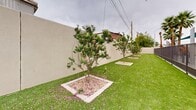 Located at 6819 N 27th Ave in Phoenix, Arizona, this single-level outdoor space offers a well-maintained courtyard designed for functional outdoor use. The grounds are landscaped with lush artificial turf that extends the length of the property, providing a clean, low-maintenance green surface throughout. A row of ornamental flowering trees — each set within defined square gravel beds framed by concrete borders — lines the perimeter, adding natural beauty and a structured aesthetic to the space. The trees, which display pink blossoms, contribute color and shade while complementing the neutral tones of the surrounding stucco privacy walls. One end of the courtyard transitions into a paved concrete area that serves as a dedicated seating zone, equipped with metal benches and a green water fountain station. A trash receptacle and an iron fence section further define this utility area, making it suitable for gathering and rest. The enclosing perimeter walls provide privacy and a sense of enclosure, creating a calm, sheltered environment despite its urban setting. The overall design balances practicality with greenery, making this outdoor courtyard a welcoming and functional space for daily use in the heart of Phoenix.