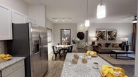 This single-story residence at The Lodges On English Station offers a thoughtfully designed open-concept layout that seamlessly connects the kitchen, dining, and living areas. The kitchen serves as a central hub, outfitted with granite countertops, a large island with bar seating, two-tone cabinetry featuring white upper and sage-gray lower cabinets, a classic subway tile backsplash, and a full suite of stainless steel appliances. Pendant lighting overhead and a dedicated pantry add both function and style. The adjacent dining area accommodates a round table beneath track lighting, while the living room features wood-look flooring, a ceiling fan, and access to natural light through large windows and glass doors. The bedrooms offer plush carpeting, ceiling fans, and ample closet space with built-in wire shelving systems. One bedroom benefits from generous natural light through multiple windows. The bathroom is finished with wood-look tile flooring, granite-topped vanity, and a walk-in glass-enclosed shower with clean tile surround. Neutral tones and consistent finishes throughout give the space a cohesive, contemporary ambiance.