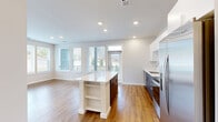 Located at 2500 Vantage Dr in Woodbridge, VA, this well-appointed 2-bedroom, 3-bathroom home offers a thoughtfully designed single-floor layout. The open-concept living, dining, and kitchen area serves as the heart of the home, bathed in natural light from large, wrap-around windows that offer outdoor views. The kitchen is outfitted with stainless steel appliances, white upper cabinetry, a tile backsplash, dark lower cabinets, and a central island with a white quartz countertop and built-in shelving — ideal for both cooking and casual dining. Warm hardwood-style flooring flows throughout the main living areas, complemented by recessed lighting overhead. The bedrooms feature plush carpeting, ceiling fans, and windows that frame natural greenery. The primary bedroom is generously sized and includes a walk-in closet with extensive wire shelving for organized storage. The bathrooms are finished with clean, modern fixtures, including a tiled soaking tub and shower combination, a floating vanity with a white countertop, and hardwood-style flooring. Additional spaces include a combined bathroom and laundry room, a utility room, and multiple closets throughout, ensuring ample storage across the entire home.