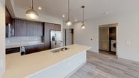 Located at 10130 Foothill Blvd in Rancho Cucamonga, CA, this thoughtfully designed single-floor residence offers a contemporary aesthetic with clean lines and modern finishes throughout. The open kitchen is a standout feature, showcasing rich wood-toned cabinetry, white quartz countertops, a large center island with an undermount sink and pendant lighting, and a full suite of stainless steel appliances including a gas range, microwave, and French door refrigerator. Light wood-look flooring flows through the main living and kitchen areas, lending a bright, cohesive feel to the space. The bedrooms are carpeted for comfort and each is equipped with a ceiling fan; several rooms feature windows with slatted blinds that allow natural light while offering views of the surrounding landscape, including palm trees. The primary bathroom is elegantly appointed with a walk-in glass shower clad in white subway tile, a dark wood vanity with white countertop, and a large LED-backlit mirror. A secondary bathroom features a full tub-shower combination with matching white tile surround and light wood-look flooring. The neutral color palette of warm grays and whites throughout creates a calm, modern ambiance well-suited for comfortable everyday living.