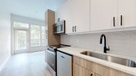 This well-appointed 1-bedroom, 1-bathroom residence offers a thoughtfully designed single-floor layout that maximizes functionality and modern style. Light hardwood flooring runs throughout the space, creating a warm, cohesive aesthetic against the clean white walls and abundant natural light.

The open-concept kitchen and living area serves as the heart of the home. The kitchen is outfitted with a full suite of stainless steel appliances, including an electric range, built-in microwave, dishwasher, and refrigerator. Two-tone cabinetry pairs white upper cabinets with warm wood-grain lower cabinets, accented by matte black hardware. A quartz countertop and subway tile backsplash complete the refined look, alongside a stainless steel undermount sink with a striking black pull-down faucet.

A bright hallway connects the living area to the private bedroom, which is a comfortable size and features large windows that invite generous natural light. A ceiling fan adds to the room's practicality, and an adjacent closet provides dedicated storage.

The bathroom is finished with large-format floor tile, full-height wall tile surrounding the soaking tub and shower combination, a wood-tone vanity with a white countertop, and a dark-framed mirror — all consistent with the home's modern design language.