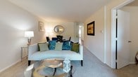 Located at 5 Stonewain Court in Towson, Maryland, this single-floor residence offers a well-organized layout designed for comfortable everyday living. The open living and dining area is finished with soft wall-to-wall carpeting and neutral tones throughout, creating a bright and inviting atmosphere. A curved sofa, glass coffee table, and oval mirror accent the living space, which flows naturally into a connected dining area. The kitchen features warm wood cabinetry, dark granite-style countertops, a black range, and hardwood-style flooring, providing a practical and efficient cooking space. Multiple bedrooms are thoughtfully sized, each with plush carpeting, built-in closets, and a calm, neutral color palette. The primary bedroom includes a walk-in closet and ample space for a full furniture arrangement, while additional bedrooms offer flexibility for guests or additional occupants. The bathrooms are clean and functional, featuring white tile surround tub-shower combinations, wood-tone vanity cabinetry, and hardwood-style flooring. Natural light filters through the windows, contributing to the overall warmth and livability of the home. The residence presents a cohesive, move-in-ready environment suited for a range of lifestyles.
