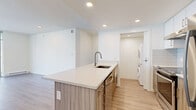 Located in New Westminster, BC, this modern multi-bedroom unit offers a well-designed, single-floor layout with a clean, contemporary aesthetic throughout. Light hardwood flooring flows continuously across the living spaces, complementing the crisp white walls and recessed lighting that keep the interiors bright and airy.

The open-concept kitchen serves as a functional centerpiece, anchored by a large island with a light quartz countertop, an undermount sink with a brushed nickel faucet, wood-grain cabinetry, and an integrated dishwasher. A dedicated in-unit laundry closet with a stacked washer and dryer adds everyday convenience.

The living area benefits from floor-to-ceiling windows and a sliding glass door that opens to a balcony, filling the space with natural light and providing open views of the surrounding neighbourhood. Baseboard heating is present throughout the unit.

The primary bedroom features mirrored sliding closet doors and direct access to one of the two bathrooms, which is outfitted with a wide vanity, quartz countertop, wood-grain cabinetry, and a large mirror. The additional bedrooms are well-proportioned, each with light flooring and sliding or hinged closet access. A hallway connects the rooms in a logical, efficient layout. The unit presents a move-in ready, modern living environment suited for a variety of occupants.