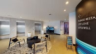 This contemporary multi-use building presents a thoughtfully designed interior that blends modern aesthetics with functional spaces across its floor. The welcoming lobby sets the tone with polished concrete floors, stone-clad elevator banks, recessed lighting, and a comfortable seating area anchored by a patterned area rug and black accent furniture. A prominent staircase with glass railings and a curved wooden banister connects levels, while bold signage and curated artwork add character to the corridors.

The lounge and social area is a standout feature, showcasing rich hardwood floors, a dramatic floor-to-ceiling textured fireplace wall with a wall-mounted flat-screen TV, and expansive floor-to-ceiling windows that frame sweeping ocean and palm tree views. Pendant lighting illuminates a dining and bar area with high-top seating, creating an inviting atmosphere for gathering.

A large, open multipurpose room—flooded with natural light from generous glazed walls overlooking the ocean—offers flexible space for events or fitness activities. A striking curved black slat partition wall adds an architectural focal point. Throughout, the design balances clean lines, warm wood tones, and cool gray palettes to create a cohesive, upscale coastal ambiance.