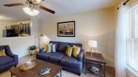This single-floor residence on Forestdale Drive in Burlington, North Carolina, offers a well-designed layout across multiple rooms, each with distinct character and practical features. The living room serves as a welcoming gathering space, centered around a plush navy-blue sofa accented with gold and teal throw pillows. Natural light pours in through large windows with sheer curtains, while framed artwork and a ceiling fan complete the relaxed atmosphere. The kitchen is equipped with dark cabinetry, black appliances including a refrigerator, electric range, and dishwasher, alongside light-toned countertops and a double sink. Wood-look flooring adds warmth underfoot. The bedrooms each carry their own personality — one features a bold olive-green accent wall, ceiling fan, and a large mirror, while another showcases a deep plum accent wall with a walk-in closet. Both rooms are carpeted and fitted with ceiling fans for year-round comfort. The bathroom includes a combination tub and shower, wood-look flooring, and warm neutral wall tones. Throughout the home, textured ceilings, ceiling fans in every room, and abundant window placements contribute to a bright, comfortable, and cohesive living environment.