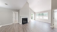 Located at 7139 Rock Ridge Ln in Alexandria, VA, this two-floor home offers a thoughtfully designed interior with a clean, neutral aesthetic throughout. The main living area immediately impresses with its dramatic vaulted ceilings that amplify the sense of space and openness. A classic wood-burning fireplace with a white-trimmed surround serves as the room's focal point, while sliding glass doors open to an outdoor balcony and large windows invite generous natural light and views of surrounding greenery. Light wood-style flooring runs through the main living spaces, adding warmth and continuity. The kitchen is well-appointed with white upper cabinetry, gray lower shaker-style cabinets, crisp white quartz countertops, a tile backsplash, stainless steel appliances, and a peninsula with an undermount sink — ideal for both cooking and casual dining. The bedrooms are carpeted for comfort, with multiple windows offering natural light and outdoor views. Bathrooms are finished with white tile surround tub-shower combinations, wood-look flooring, and white vanities. One bathroom features built-in closet shelving adjacent to the vanity area. The second floor, accessible via an interior staircase, extends the home's versatile living options.
