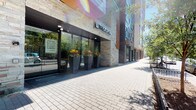 Located within The Aspen, a contemporary residential building with a striking exterior of stone cladding and floor-to-ceiling glass, this single-floor unit offers a thoughtfully designed interior with a clean, modern aesthetic. The building's street-level entrance is welcoming, featuring curated landscaping with bold planters and a well-maintained paved walkway.

Inside the unit, warm hardwood-style flooring runs throughout, complementing the cool gray-toned walls and crisp white trim. One of the most distinctive design elements is the frosted glass sliding barn door, which adds a stylish, semi-transparent partition between spaces while allowing natural light to filter through — a detail that balances privacy with an open feel.

The unit includes an in-unit stacked washer and dryer, a practical and convenient amenity tucked neatly into a dedicated space. The full bathroom features a bathtub and shower combination, a toilet, and a towel bar, all finished in a simple, clean style consistent with the rest of the unit.

Natural light plays a notable role in the ambiance, with sunlight casting bright, angled patterns across the walls and floors. The overall layout is functional and well-proportioned, with multiple doorways connecting the spaces in a straightforward, easy-to-navigate flow. The unit presents a polished, move-in-ready environment suited to modern urban living.