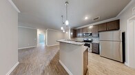 Located at 117 Dawson Ave in Dawsonville, Georgia, this well-appointed single-story home offers four bedrooms, two full bathrooms, and a thoughtfully designed layout. The interior is finished with warm wood-look luxury flooring throughout the main living areas and select bedrooms, complemented by neutral-toned walls and clean white trim that create a bright, cohesive aesthetic.

The kitchen is equipped with stainless steel appliances, including a refrigerator, range, and microwave, along with rich dark-stained cabinetry and granite countertops. It opens conveniently toward the dining and living areas, promoting an easy flow for everyday living. The living room features crown molding, a ceiling fan with light, and French doors that invite natural light and outdoor access.

The spacious primary bedroom is carpeted for comfort and includes a walk-in closet with built-in shelving. Its en-suite bathroom boasts a double-sink vanity with granite countertops, dark cabinetry with brushed nickel hardware, and a separate shower area. The secondary bathroom mirrors the same quality finishes, featuring a tub-shower combination and a single-sink granite vanity.

Additional bedrooms offer wood-look flooring and crown molding details. A dedicated laundry room houses side-by-side washer and dryer units with overhead shelving for added storage. Three closets throughout the home provide ample organizational space.