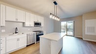 Located at 932 Maple Ave in Downers Grove, Illinois, this single-floor unit showcases a clean, contemporary design with thoughtful finishes throughout. The kitchen serves as a central highlight, featuring white shaker cabinetry, a white subway tile backsplash, light quartz countertops, and a full suite of stainless steel appliances including a gas range, built-in microwave, dishwasher, and refrigerator. A substantial center island provides additional prep and seating space, illuminated overhead by an industrial-style pendant light fixture with glass bulbs. Wood-look flooring runs throughout the main living areas, adding warmth to the modern palette.

Sliding glass doors connect the living area directly to a private balcony, allowing natural light to pour into the space and offering outdoor views. The bedrooms feature neutral-toned carpet, large windows, and clean wall finishes that create a calm, functional environment. One bedroom also includes direct balcony access via a sliding glass door. The bathroom is finished with classic white subway tile surrounding a soaking tub and shower combination, complemented by wood-look flooring and simple chrome fixtures. Overall, the unit presents a bright, move-in-ready living environment with modern, cohesive finishes.