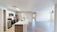 This 1,240-square-foot, single-story apartment at MacAlpine Place offers a thoughtfully designed 3-bedroom, 2-bathroom layout. The open-concept kitchen and living area serves as the heart of the home, featuring a large center island with a undermount sink, quartz countertops, white shaker-style upper cabinets, sage-toned lower cabinets, a subway tile backsplash, and a full suite of stainless steel appliances including a refrigerator, range, and over-the-range microwave. The spacious living room is finished with wood-look luxury vinyl plank flooring, neutral warm-toned walls, and a ceiling fan with light fixture, with natural light provided by multiple windows dressed with horizontal blinds. The three bedrooms each feature the same wood-look flooring and windows overlooking the outdoors. The primary bedroom measures 170 square feet and includes access to a dedicated closet with wire shelving systems. The two bathrooms are finished with gray vanity cabinets, quartz countertops, undermount sinks, and black hardware accents. One bathroom includes a window for added natural light. Three total closets provide generous storage throughout the unit, and a hallway connects the private bedroom wing to the main living areas.