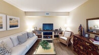 Located at 1060 Coral Ridge Dr in Coral Springs, FL, this single-floor, three-bedroom, two-bathroom residence offers a well-designed layout with a warm and inviting coastal aesthetic throughout. The living room provides a comfortable gathering space with wood-look flooring, neutral-toned walls, and soft ambient lighting, complemented by coastal-inspired wall art and built-in shelving. Adjacent to the living area, the dining room features natural light from a window with sheer curtains and a ceiling fan overhead, creating a bright and airy atmosphere. The kitchen is well-appointed with dark espresso cabinetry, granite countertops, stainless steel appliances including a refrigerator, dishwasher, and microwave, and light wood-look tile flooring. The primary bedroom is spacious, featuring a tufted headboard, ceiling fan, natural light from a window with linen drapes, and wood-look flooring. The en-suite bathroom includes a large mirrored sliding door closet, a vanity with dark cabinetry and white countertops, and a walk-in shower. The additional bedrooms are equally well-appointed, each with ceiling fans, ample natural light, mirrored closets, and consistent wood-look flooring, maintaining the cohesive and polished design throughout the home.