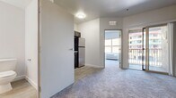 This efficient one-bedroom, one-bathroom unit is thoughtfully laid out across a single floor, offering a practical and functional living arrangement. The living area features soft wall-to-wall carpeting and neutral-toned walls that create a clean, understated aesthetic. A sliding glass door leads to a private balcony, filling the space with natural light and providing views of the surrounding exterior.

The kitchen is compact yet well-appointed, featuring dark espresso cabinetry with ample upper and lower storage, light stone-look countertops, and a full suite of stainless steel appliances including a refrigerator, range, and built-in microwave. Wood-look plank flooring grounds the kitchen area, providing a clean contrast to the carpeted living space.

The bedroom is a cozy, carpeted retreat with a large window that admits generous natural light and houses a wall-mounted HVAC unit for individualized climate control. The room's simple layout provides flexibility for various furniture arrangements.

The bathroom is finished with wood-look tile flooring and features a sleek dark-framed vessel sink vanity with a glass countertop, a framed mirror above, and a full soaking tub and shower combination with clean white surrounds. Together, these elements create a cohesive and modern feel throughout the unit.