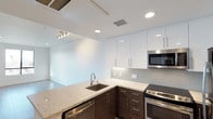 Located at 986 Broadway in Chula Vista, unit B305 is a single-floor residence showcasing a contemporary design aesthetic throughout. The kitchen serves as a central highlight, featuring a striking two-tone cabinet scheme with dark espresso lower cabinets contrasting elegantly against crisp white upper cabinetry. Light-toned granite countertops extend across the workspace, including a peninsula that provides additional prep space and opens toward the living area, enhancing the sense of flow and connectivity. A mosaic tile backsplash adds textural interest behind the range, while stainless steel appliances — including a built-in microwave, electric range, and dishwasher — complete the modern culinary space. Recessed lighting is thoughtfully distributed across the white ceiling, complemented by a track lighting fixture in the adjoining living area, ensuring the space is well-lit throughout. The open-concept layout connects the kitchen seamlessly to the living area, which features clean white walls and polished flooring, contributing to a bright and airy atmosphere. The overall design reflects a clean, minimalist sensibility well-suited to modern living.