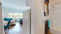 Located at 3220 Federal Blvd in Denver, Colorado, this single-floor unit offers a clean, contemporary design with an open and efficiently arranged layout. Warm-toned hardwood-style flooring runs throughout the space, creating a cohesive and inviting atmosphere from room to room.

The living area is bright and airy, anchored by a large window that fills the space with natural light and provides views of surrounding greenery. The kitchen is seamlessly integrated into the main living space and features white cabinetry, white appliances including a range, microwave, and refrigerator, a stainless steel sink, and a dishwasher. Ample counter space and a built-in closet with shelving offer practical storage solutions.

The sleeping area is generously proportioned, accommodating a full bed alongside a built-in desk workspace and a separate closet. A large window brings in additional natural light and outdoor views, enhancing the sense of openness.

The bathroom is well-appointed with a full soaking tub and shower combination, finished with clean white subway tile surround, wood-style flooring, and a built-in niche shelf for storage. The overall aesthetic throughout is modern and minimal, with white walls providing a neutral, versatile backdrop.