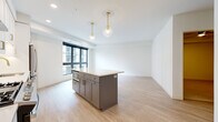 This well-appointed single-floor residence offers three bedrooms, two bathrooms, and a thoughtfully designed open-concept layout. The kitchen and living area flow seamlessly together, anchored by a standout kitchen featuring a central island with a gray base and white quartz countertop, floor-to-ceiling white shaker cabinetry with gold hardware, stainless steel appliances including a gas range, French door refrigerator, and dishwasher, complemented by a subway tile backsplash and a stainless steel hood vent. Elegant globe pendant lights with brass fixtures add a refined touch overhead. Light wood-tone flooring runs throughout the main living areas, lending warmth to the clean, neutral palette. The living room offers direct access to a balcony through large black-framed glass doors, filling the space with natural light and outdoor views of the surrounding building. The bedrooms are bright and airy, each featuring large black-framed windows and soft carpeting in the primary suite. The two bathrooms are finished with white shaker vanities, matte black fixtures, and warm-toned countertops. Two closets provide additional storage. The overall aesthetic is clean and contemporary, with a cohesive modern design throughout.