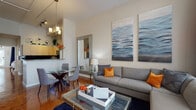 Located in the Baldwin Park neighborhood of Orlando, this single-floor residence offers a thoughtfully designed layout with modern finishes throughout. The open-concept living and dining area is anchored by a spacious sectional sofa, a glass coffee table, and striking large-format wall art, all bathed in natural light from tall windows dressed with floor-length drapes. Rich polished concrete flooring runs throughout the home, adding warmth and character to every room.

The kitchen is well-appointed with light wood cabinetry extending to the ceiling for ample storage, granite countertops, a bold navy tile backsplash, and a full suite of stainless steel appliances including a range, built-in microwave, and sink. The bedroom is a serene retreat featuring soaring ceilings, large windows that invite abundant natural light, and direct access to an outdoor area. The full bathroom includes a tub-shower combination, wood-toned cabinetry, and dark stone countertops. A dedicated in-unit laundry area with a full-size washer and dryer adds everyday convenience. The cohesive color palette of navy, orange, and neutral tones lends the space a polished, contemporary ambiance throughout.
