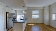Located at 205 Church Street in the heart of New Haven, CT, this one-bedroom, one-bathroom unit offers a well-designed single-floor layout with a bright, modern aesthetic. The open-concept living and kitchen area is anchored by warm hardwood flooring that runs throughout, creating a cohesive and inviting atmosphere. The kitchen is outfitted with white cabinetry, dark stone countertops, and stainless steel appliances including a gas range and microwave. A peninsula with an undermount sink provides additional prep space and serves as a natural divider between the kitchen and living area. Two pendant lights hang above the peninsula, adding focused illumination and a stylish touch. Large windows with horizontal blinds flood the space with natural light and frame elevated views of the New Haven cityscape, enhancing the sense of openness. The clean white walls and minimalist trim work contribute to the unit's contemporary feel. The thoughtful layout maximizes functionality within a comfortable footprint, making efficient use of every square foot. This unit combines urban convenience with polished interior details in one of New Haven's central locations.