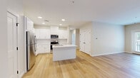 Located in Boylston, MA, this thoughtfully designed 2-bedroom, 2-bathroom residence offers a modern, single-floor layout with a clean, contemporary aesthetic. Light-toned hardwood flooring runs throughout the entire space, creating visual continuity and a warm, inviting ambiance.

The open-concept kitchen and living area serves as the heart of the home. The kitchen is outfitted with crisp white shaker cabinetry, white quartz countertops, a central island with an undermount sink, and a full suite of stainless steel appliances including a refrigerator, range, and over-the-range microwave. Recessed lighting illuminates the space from above, enhancing its bright, airy feel.

The spacious primary bedroom features large windows overlooking lush tree-lined surroundings, allowing generous natural light to fill the room. It includes a double-door closet for ample storage. The second bedroom is equally well-lit and features the same consistent hardwood flooring and neutral wall tones.

Both bathrooms are finished in a clean, minimal style. One bathroom features a walk-in glass-enclosed shower, tile flooring, and a window that brings in natural light. Throughout the residence, white panel doors with matte black hardware provide a refined contrast to the neutral palette, lending a polished, modern character to every room.