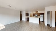 This single-floor residence offers a thoughtfully designed open-concept layout that seamlessly connects the living and kitchen areas. The spacious living room is bathed in natural light, courtesy of large windows that overlook the surrounding exterior, and features light-toned hardwood-style flooring that extends throughout the common areas. A set of sliding glass doors provides additional access to the outdoors, enhancing the bright, airy atmosphere.

The kitchen serves as a functional centerpiece, equipped with stainless steel appliances including a refrigerator, electric range, and microwave. Rich, dark cabinetry pairs with light countertops to create a modern contrast, while pendant lighting above the kitchen island adds a stylish touch. A dedicated pantry offers generous storage just steps from the cooking area.

The bedrooms are carpeted for comfort and include windows that allow natural light to filter in. The primary bathroom features a dual-sink vanity with a white countertop, dark cabinetry, a large mirror with vanity lighting, and access to a walk-in closet. A second bathroom offers a clean, efficient layout with a tub-shower combination, single-sink vanity, and matching contemporary finishes. Textured accent walls in select areas add subtle architectural character throughout the residence.