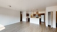 This single-floor residence offers a thoughtfully designed open-concept layout that seamlessly connects the living and kitchen areas. The spacious living room is bathed in natural light, courtesy of large windows that overlook the surrounding exterior, and features light-toned hardwood-style flooring that extends throughout the common areas. A set of sliding glass doors provides additional access to the outdoors, enhancing the bright, airy atmosphere.

The kitchen serves as a functional centerpiece, equipped with stainless steel appliances including a refrigerator, electric range, and microwave. Rich, dark cabinetry pairs with light countertops to create a modern contrast, while pendant lighting above the kitchen island adds a stylish touch. A dedicated pantry offers generous storage just steps from the cooking area.

The bedrooms are carpeted for comfort and include windows that allow natural light to filter in. The primary bathroom features a dual-sink vanity with a white countertop, dark cabinetry, a large mirror with vanity lighting, and access to a walk-in closet. A second bathroom offers a clean, efficient layout with a tub-shower combination, single-sink vanity, and matching contemporary finishes. Textured accent walls in select areas add subtle architectural character throughout the residence.