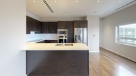 This two-bedroom, two-and-a-half-bath penthouse delivers a refined living experience with modern finishes and thoughtful design throughout. Rich hardwood flooring flows continuously across the open-plan layout, complemented by recessed lighting and ceiling fans in each bedroom. The living and dining area is bathed in natural light through a generous bank of windows framing sweeping panoramic city views, creating an airy, elevated atmosphere.

The chef's kitchen is a standout feature, appointed with dark espresso cabinetry reaching toward the ceiling, a large center island with a light quartz countertop and undermount sink, stainless steel appliances including a double wall oven, microwave, and French door refrigerator, and a clean tile backsplash. The kitchen opens seamlessly to the main living area, making it ideal for entertaining.

The primary suite includes direct access to a luxurious en-suite bathroom finished in white mosaic tile, featuring a double-sink vanity with backlit mirrors, a freestanding soaking tub, and a glass-enclosed shower. A spacious walk-in closet with adjustable shelving and hardwood floors provides ample storage. The second bedroom is generously sized with its own en-suite bath. A stylishly appointed half bath with a pedestal sink serves guests.