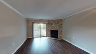 This single-floor residence offers a well-appointed layout with a blend of functional design and comfortable living spaces. The main living area is a standout, showcasing rich dark hardwood flooring, crown molding, and a striking floor-to-ceiling stacked stone fireplace as the focal point. A sliding glass door with vertical blinds opens to a balcony, allowing natural light to fill the room and providing outdoor views of surrounding greenery.

An adjacent open area, also finished with hardwood flooring and crown molding, features a ceiling fan and connects seamlessly to the rest of the unit via a central corridor. The kitchen is well-equipped with white shaker-style cabinetry, dark countertops, a subway tile backsplash, and stainless steel appliances, including a range and over-the-range microwave. A window above the counter brings in natural light.

The bedrooms are carpeted for comfort, each offering sliding-door closets and access to natural light. One bedroom features a sliding glass door opening to a private balcony with tree-lined views. The bathroom includes a single-sink vanity with dark countertops, white cabinetry, and a tub-shower combination, completing this practical and well-designed residence.