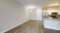 This single-floor residence at Alta Towne Lake in Pooler, Georgia, offers a well-designed layout finished with consistent wood-look flooring and neutral warm-beige walls throughout. The open living and dining area is a central highlight, featuring a ceiling fan, a pendant light fixture, and a sliding glass door fitted with vertical blinds that allows natural light to fill the space and provides access to an outdoor area. The layout flows naturally from the living area toward the entry, where a front door is visible from the dining zone.

The kitchen is designed for functionality, featuring white cabinetry, granite-look countertops, and a full suite of stainless steel appliances, including a side-by-side refrigerator with an ice and water dispenser, a built-in microwave, and an electric range. The galley-style configuration maximizes efficiency within the available space.

A secondary room, suitable as a bedroom or office, includes a ceiling fan with light kit and a window overlooking outdoor greenery, bringing in natural light. The bathroom is equipped with a soaking tub and tiled shower surround, white cabinetry with granite countertops, and wood-look flooring that continues the cohesive aesthetic found throughout the residence.