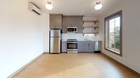 This single-floor unit offers a thoughtfully designed layout with a clean, modern aesthetic throughout. Light-toned hardwood flooring flows seamlessly across the main living areas, creating a warm and cohesive feel.

The kitchen is a standout feature, outfitted with gray shaker-style cabinetry, white quartz countertops, and a classic white subway tile backsplash. A full suite of stainless steel appliances — including a refrigerator, electric range, over-the-range microwave, and dishwasher — provides everything needed for everyday cooking. Open wood shelving adds a contemporary touch, and a window allows natural light to fill the space. A wall-mounted mini-split unit ensures efficient climate control.

The bathroom is clean and functional, featuring a full tub-shower combination, a white vanity with ample counter space, and neutral tile flooring. Its streamlined design prioritizes practicality without sacrificing comfort.

A dedicated in-unit laundry closet houses a stacked washer and dryer, conveniently tucked behind louvered doors. A walk-in closet provides generous storage, while the overall layout — visible in the dollhouse view — reflects an efficient and well-organized floor plan. The space is freshly finished and move-in ready.