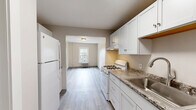 Located at 1101 Elm St in Manchester, NH, this efficient one-bedroom, one-bathroom unit offers a well-organized single-floor layout. Light gray luxury vinyl plank flooring runs throughout, providing a clean, cohesive look across all rooms.

The galley-style kitchen is thoughtfully designed with white shaker cabinetry extending to the upper walls, granite countertops, a stainless steel sink, and white appliances including a gas range and full-size refrigerator. Ample cabinet storage makes the most of the streamlined layout, and a doorway at the end of the kitchen leads to a closet and entry door.

The bedroom is a comfortable, well-proportioned room featuring a large double-hung window that invites natural light and offers views of the surrounding neighborhood. A traditional cast-iron radiator provides reliable heating, a nod to the building's classic character.

The bathroom features a white vanity with a light stone-topped countertop and brushed nickel hardware and fixtures, maintaining a clean, modern aesthetic. A hallway connecting the bathroom to the rest of the unit includes additional storage space.

Neutral warm-beige wall tones throughout complement the light flooring and white trim, creating a bright and cohesive interior. The overall design balances classic architectural elements with updated finishes.