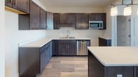 Located at 1185 Shelburne Road in Burlington, Vermont, this single-floor unit offers a thoughtfully designed layout with modern finishes throughout. The kitchen is a standout feature, outfitted with rich dark-stained cabinetry, light quartz countertops, stainless steel appliances including a dishwasher and microwave, a double-basin sink, and durable wood-look flooring. A dedicated pantry closet with built-in wire shelving provides convenient additional storage just steps from the kitchen. The open living and dining areas continue the wood-look flooring and are bathed in natural light, with a wall-mounted mini-split unit offering efficient climate control. Carpeted bedroom spaces offer a comfortable, quiet retreat, with large windows framing outdoor views of the surrounding Burlington landscape. Interior doors feature classic raised-panel detailing, and clean white trim and baseboards run throughout, lending a crisp, cohesive aesthetic. The bathroom includes a full soaking tub and shower combination with chrome fixtures, tile-look flooring, and access to a closet for added convenience. Overall, the space presents a clean, contemporary feel with a neutral palette that provides a versatile backdrop for a variety of interior styles.