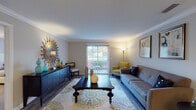 This single-floor residence offers a thoughtfully designed layout that balances comfort and functionality across its key living spaces. The living room serves as the heart of the home, showcasing crown molding, wood-look flooring, and a sliding glass door that opens to an outdoor balcony, allowing natural light to fill the room. A bold starburst mirror accent wall, a tufted gray sofa, and a patterned area rug contribute to the space's inviting character.

Adjacent to the living room, the dining area features crown molding, wood-look flooring, and a pendant light fixture overhead, with direct visual access to the kitchen. The galley-style kitchen is well-equipped with white shaker cabinetry, marble-look countertops, subway tile backsplash, stainless steel appliances, and wood-look tile flooring, offering an efficient and clean workspace.

The two bedrooms are carpeted and comfortably scaled, each with windows that provide natural light. The primary bedroom includes ample space for a dresser and bed. The full bathroom features a marble-look vanity countertop, a combined tub and shower with a chevron-patterned curtain, and wood-look tile flooring, completing this well-rounded residence.
