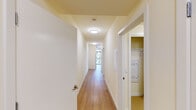 This well-appointed single-floor residence offers a clean, contemporary design throughout, with warm hardwood-style flooring connecting the main living areas and a neutral color palette that enhances the sense of light and openness. The layout is thoughtfully organized, beginning with a bright, spacious hallway that leads to the various rooms of the unit, with in-unit laundry conveniently accessible off the corridor.

The open-concept living and dining area is a standout feature, characterized by a striking corner configuration of floor-to-ceiling windows that flood the space with natural light and frame panoramic views of the surrounding urban landscape. The kitchen is positioned adjacent to the living area and is outfitted with a full suite of stainless steel appliances — including a refrigerator, electric range, microwave, and dishwasher — complemented by light wood cabinetry, a built-in sink, and track lighting overhead.

Two bedrooms provide comfortable private retreats, each finished with plush carpeting, crisp white walls, and windows with blinds offering views of the cityscape. The overall ambiance of the space is bright, clean, and move-in ready, with a modern aesthetic that balances functionality and comfort throughout.
