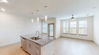 Located at 8025 Monty Stratton Pkwy in Greenville, Texas, this thoughtfully designed single-story residence offers a clean, modern aesthetic throughout its efficiently laid-out floor plan. Light wood-style flooring flows through the main living areas, complementing the bright, neutral color palette that gives the space an open and airy feel.

The open-concept kitchen and living room serve as the heart of the home. The kitchen is outfitted with gray shaker-style cabinetry, stainless steel appliances including a refrigerator, range, and built-in microwave, and a central island topped with granite countertops. Stylish pendant lighting hangs above the island, adding a modern touch. The layout allows for seamless interaction between the kitchen and living areas.

The bedroom features plush carpet flooring, a ceiling fan, and multiple windows dressed with blinds that invite natural light and outdoor views of the surrounding greenery. A dedicated walk-in closet with built-in shelving and hanging rods provides ample storage. A separate laundry room accommodates a full-size washer and dryer.

The bathroom is finished with a granite-topped vanity with gray cabinetry, light wood-look tile flooring, and a soaking tub with a tiled surround and sliding glass enclosure, combining both comfort and style.