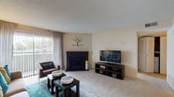 This well-appointed single-floor residence at Alton Green offers a thoughtfully designed layout that balances comfort and functionality across its key living spaces. The living room serves as the heart of the home, featuring plush wall-to-wall carpeting, a striking dark brick fireplace as a focal point, and a sliding glass door framed by vertical blinds and sheer curtains that invite natural light while offering views to the outdoors. The seating area is generously sized, providing ample room for relaxing and entertaining. Adjacent to the living room, the galley-style kitchen is equipped with dark espresso cabinetry, light countertops, and a full suite of appliances including a stainless steel refrigerator and black range. Rich hardwood-style flooring grounds the space, adding warmth and contrast to the cabinetry. The bedroom is a serene retreat, carpeted for comfort, with a large window that draws in natural light and offers outdoor views. Closet storage is conveniently accessible from within the room. The bathroom features hardwood-style flooring, a full tub and shower combination with clean white tile surround, and a vanity with dark cabinetry that complements the home's cohesive design aesthetic throughout.