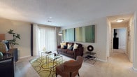 Located at 991 Wylie Rd in Marietta, Georgia, this single-floor residence offers a thoughtfully designed layout with comfortable living spaces and modern finishes throughout. The living room is a welcoming centerpiece, featuring plush wall-to-wall carpeting, a textured ceiling, and a large sliding glass door dressed with vertical blinds that fills the room with natural light and provides access to the outdoors. The galley-style kitchen is both functional and stylish, boasting rich dark wood cabinetry, granite-style countertops, wood-look flooring, and black appliances including a refrigerator, range, and dishwasher — offering ample storage and prep space. The residence includes multiple bedrooms, each carpeted and well-lit, with generous windows that bring in natural light and views of the surrounding greenery. The bathrooms are finished with wood-look flooring, white cabinetry, granite-style vanity tops, large mirrors, and tiled tub-shower combinations, presenting a clean and contemporary aesthetic. Neutral warm tones carry throughout the home, lending a cohesive and inviting ambiance. The overall layout, as seen from the dollhouse view, reveals a well-organized floor plan with distinct living, dining, kitchen, and sleeping areas, making this a practical and comfortable space in the heart of Marietta.