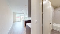 This well-appointed single-floor unit offers a thoughtfully designed open-concept layout that maximizes its compact footprint. The combined kitchen and living area serves as the heart of the space, featuring light wood-tone flooring throughout that lends warmth and visual continuity.

The kitchen is a standout feature, showcasing rich dark-wood cabinetry extending to the ceiling for ample storage, paired with crisp white quartz countertops and a large peninsula with an integrated sink. Pendant lighting hangs above the peninsula, adding both style and function. Stainless steel appliances — including a French door refrigerator, range, built-in microwave, and dishwasher — complete the modern culinary space. A white subway tile backsplash adds a clean, contemporary accent.

The living area is bright and airy, benefiting from floor-to-ceiling sliding glass doors that open onto a private balcony with outdoor views, allowing abundant natural light to flood the interior.

The bathroom features large-format gray tile flooring, a full soaking tub with tiled surround, a warm wood vanity with a white countertop, and a backlit mirror, all contributing to a clean, spa-like atmosphere throughout.