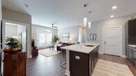Located at 7870 Alta Dr. in Columbus, Ohio, this single-floor residence offers a thoughtfully designed open-concept layout that seamlessly connects the kitchen, dining, and living areas. The kitchen is a standout feature, showcasing a large center island with a white quartz countertop, undermount sink, and seating for multiple bar stools. Dark espresso cabinetry reaches toward the ceiling, providing ample storage, while stainless steel appliances — including a refrigerator, microwave, and range — add a sleek, modern touch. Stylish pendant lights hang above the island, complementing the recessed ceiling lighting throughout. Rich, dark hardwood-style flooring flows through the main living areas, creating a warm and cohesive aesthetic. The living room is bright and inviting, featuring large windows and a glass-paneled door that flood the space with natural light, along with a ceiling fan for added comfort. The bedroom offers plush carpeting, multiple windows, and a serene, neutral color palette. The bathroom is well-appointed with dark wood vanity cabinetry, a white countertop, framed mirror, and a glass-enclosed shower. Neutral gray tones on the walls throughout lend a calm, contemporary ambiance to the entire residence.