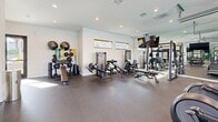 Located at 2420 Cardinal Drive in San Diego, CA, this well-appointed fitness center offers a thoughtfully designed single-floor exercise space. The room is finished with durable rubber flooring throughout, providing a safe and functional surface ideal for a wide range of workouts.

The cardio zone is equipped with multiple treadmills, elliptical trainers, and a stationary cycle, all positioned along a striking glass garage-style door that floods the space with natural light and frames views of the outdoor pool and palm-lined surroundings. This open-air design element creates an inviting, energizing atmosphere.

The strength training area features a comprehensive selection of selectorized cable machines, adjustable weight benches, and a full dumbbell rack, catering to both beginner and advanced users. A large wall-to-wall mirror visually expands the space and allows for proper form checks during exercise. A wall-mounted flat-screen television is positioned prominently for entertainment during workouts.

The free weights corner includes medicine balls, resistance bands, stability balls, and a ball rack, supporting functional and accessory training. Recessed lighting throughout ensures the space is evenly and brightly lit. Clerestory windows along one wall admit additional natural light while maintaining privacy. A water fountain is conveniently accessible within the space, rounding out this comprehensive and modern fitness facility.