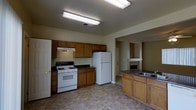 This two-floor space offers a practical and well-organized layout designed for comfortable everyday living. The kitchen is a central highlight, featuring warm honey-toned wood cabinetry that provides generous storage along the walls. A gas range with an overhead vent hood anchors the cooking area, complemented by a full-size refrigerator and dark countertops that offer a subtle contrast to the cabinetry. A kitchen island with an integrated sink adds additional workspace and convenience, making the kitchen both functional and versatile. The flooring throughout the kitchen area features a neutral tile pattern that is easy to maintain. The open sightlines from the kitchen extend toward an adjoining area where a fireplace serves as a notable architectural feature, adding warmth and character to the living space. Overhead fluorescent lighting ensures the kitchen is well-lit throughout the day. The overall ambiance of the space is straightforward and functional, with a layout that facilitates ease of movement between areas. With two floors, the property offers separation between living and other functional spaces, providing a practical and organized environment suited to a variety of needs.