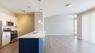 Located at 2100 Haddonfield Rd in Pennsauken, NJ, this single-floor residence offers a thoughtfully designed open-concept layout with modern finishes throughout. The living and kitchen areas flow seamlessly together, anchored by a striking kitchen island finished in bold navy blue — and in some units, a vibrant cobalt blue — with a crisp white countertop and an undermount sink. Pendant lighting hangs above the island, complementing the stainless steel appliances and light wood cabinetry. Wide-plank wood-style flooring runs throughout the main living areas, adding warmth and continuity. The spacious living area is bathed in natural light through large windows dressed with vertical blinds, creating an airy, open ambiance. The bedroom features plush carpeting, generous closet space, and oversized windows that invite abundant natural light. The bathroom is well-appointed with a sliding-glass enclosed shower, a wide vanity with light blue cabinetry, a white countertop, and wood-style flooring that ties the space together. Neutral warm-toned walls throughout the unit provide a clean, versatile backdrop. The overall design balances contemporary style with functional living in a comfortable, well-lit single-level layout.