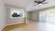 This well-appointed single-floor unit offers a clean, modern aesthetic throughout, highlighted by light wood-look flooring that flows seamlessly from room to room. The open-concept living area is bright and welcoming, anchored by a ceiling fan with integrated lighting and large sliding glass doors dressed with vertical blinds that allow abundant natural light and outdoor views to pour in.

The kitchen is thoughtfully designed with white shaker-style cabinetry, matte black hardware, white quartz countertops, and a full suite of stainless steel appliances including a refrigerator, range, microwave, and dishwasher. A pass-through counter connects the kitchen to the living area, enhancing the sense of openness and making the layout ideal for everyday living.

The bedroom is a comfortable retreat, featuring its own ceiling fan, a window with outdoor greenery views, and the same consistent light flooring found throughout the unit.

Two bathrooms round out the space with modern updates. One features a floating white vanity with a black faucet and a clean, minimalist design. The second bathroom includes a soaking tub and shower combination adorned with striking marble-look tile surround, complemented by matte black fixtures and a white vanity. Both bathrooms carry the same cohesive, contemporary character that defines this move-in ready unit.