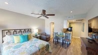 Located at 960 W Southern Ave in Mesa, Arizona, this single-floor studio presents a thoughtfully designed open-concept layout that efficiently combines sleeping, living, and dining areas into one cohesive space. Wood-look flooring runs throughout, lending warmth and continuity, while a textured ceiling and a ceiling fan with overhead lighting provide comfort and functionality.

The main living area accommodates a full-sized bed, a cozy seating arrangement, and a compact dining set, making excellent use of the available footprint. Recessed lighting and neutral gray wall tones contribute to a bright, clean atmosphere. A window allows natural light to filter in, enhancing the open feel of the room.

The kitchenette is efficiently outfitted with white shaker-style cabinetry, granite-look countertops, a coil electric cooktop, an over-the-range microwave, and a compact refrigerator—all in stainless steel finishes. Ample cabinet storage keeps the space organized and functional.

The bathroom features granite-look countertops consistent with the kitchen, recessed lighting, and a towel rack, with a hallway leading to additional closet or storage space. Clean finishes and neutral tones carry through from the main living area, maintaining a unified aesthetic throughout the entire unit.