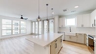 This well-appointed 2-bedroom, 3-bathroom single-story residence showcases a clean, modern design with a thoughtfully open layout. The combined kitchen and living area forms the heart of the home, featuring light hardwood-style flooring, crisp white cabinetry, a large center island with quartz countertops, and stainless steel appliances including a refrigerator, range, and built-in microwave. Geometric pendant lights hang above the island, adding a contemporary touch, while multiple windows and a glass-panel door flood the space with natural light. A ceiling fan enhances comfort throughout the living area.

The bedrooms are carpeted for warmth and comfort, each equipped with ceiling fans and generous windows that frame outdoor views. The primary bedroom connects directly to a well-designed en-suite bathroom featuring a dual-sink vanity with white quartz countertops, light tile flooring, a glass-enclosed shower, and matte black hardware accents. A spacious walk-in closet with built-in shelving and hanging rods provides excellent storage. Secondary bathrooms mirror the clean aesthetic with white vanities and bold black-framed mirrors. A bright hallway with recessed lighting connects the private areas of the home seamlessly.