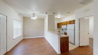 This single-story home offers a practical and comfortable layout designed for easy everyday living. The open-concept living area greets you at the front entry, featuring warm hardwood-style flooring, crisp white walls, and a ceiling fan with integrated lighting that keeps the space bright and well-ventilated. Natural light filters in through front-facing windows fitted with blinds, creating an inviting atmosphere.

The kitchen is thoughtfully positioned adjacent to the living area and is defined by a raised peninsula counter that serves as both a workspace and a casual divider between the two zones. Rich, warm-toned wood cabinetry provides generous storage, while a subtle mosaic tile backsplash adds a decorative accent. White appliances, including a range, microwave, and refrigerator, complete the functional kitchen setup. Light tile flooring in the kitchen transitions seamlessly to the hardwood-style floors of the surrounding areas.

A dedicated laundry area is accessible via a secondary door and includes upper cabinetry for additional storage. The bathroom features a wide vanity with a single sink, a large mirror, and a shower, with hardwood-style flooring carrying through for a cohesive look. The bedrooms are generously proportioned, each with its own ceiling fan, hardwood-style floors, and windows that bring in natural light, offering versatile spaces suitable for a variety of configurations.