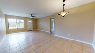 This single-story home presents a cohesive, practical layout unified by large-format ceramic tile flooring and warm beige wall tones throughout. The main living area is generously proportioned, bathed in natural light from a large front window and an arched-glass front door. A ceiling fan overhead and a pendant light fixture add functional character to the space. The open layout connects seamlessly to a dedicated dining area, also highlighted by a pendant light, with a clear sightline into the kitchen.

The kitchen features warm-toned wood cabinetry, granite countertops, a decorative tile backsplash, and white appliances including an electric range and built-in microwave. A door provides direct exterior access, adding convenience.

The bedroom wing includes rooms with closet access and hallway connectivity. One bathroom is equipped with a tiled soaking tub and surround, a wood vanity with granite countertop, and tile flooring. A second bathroom offers a walk-in tiled shower with a mosaic-tile floor inset. Both bathrooms carry the same neutral, warm palette seen throughout the home.

Overall, the space presents a clean, move-in-ready interior with consistent finishes and a straightforward, functional floor plan.