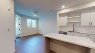 This contemporary single-floor residence offers a thoughtfully designed open-concept layout that seamlessly connects the kitchen and living area. The kitchen is a standout feature, showcasing crisp white shaker cabinetry, open shelving, a white quartz island with bar seating, a subway tile backsplash, and a full suite of stainless steel appliances including a gas range, built-in microwave, dishwasher, and a French door refrigerator. Wood-look flooring flows throughout the main living areas, complementing the clean, modern aesthetic. The living area benefits from natural light through a window fitted with horizontal blinds, while a ceiling fan adds comfort year-round. The bedroom features plush carpet, neutral walls, and access to a spacious walk-in closet. The full bathroom is finished with large-format tile flooring, a tiled tub-and-shower combination with a sliding glass door, a white vanity with an undermount sink, and black hardware accents. A hallway houses a stacked in-unit washer and dryer for added convenience. The space is completed by a private outdoor patio, offering a quiet retreat with views of the surrounding neighborhood.