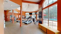 Located at 3301 Glenn McConnell Pkwy in Charleston, South Carolina, this single-floor fitness center is a well-equipped and visually striking facility designed to energize and motivate. The space is defined by bold, vibrant orange walls that lend a dynamic and high-energy atmosphere throughout. The layout is divided into distinct functional zones, seamlessly connected to create a comprehensive workout environment.

The cardio area features a vaulted, octagonal ceiling with recessed lighting and a ceiling fan, creating an airy, open feel. Floor-to-ceiling arched windows and large glass panels flood the space with abundant natural light and provide views of the outdoor pool and surrounding greenery. Multiple treadmills and elliptical machines are arranged to face the windows, enhancing the workout experience. Wall-mounted televisions offer additional entertainment.

A dedicated strength and free weights section includes cable machines, adjustable benches, weight racks with dumbbells, and various resistance equipment. Full-length mirrors line the walls, amplifying the sense of space and supporting proper form during exercise. Ceiling fans maintain comfortable airflow throughout.

A transitional lounge area with modular seating connects the fitness zones and opens through glass sliding doors to adjacent interior spaces. The combination of natural light, thoughtful equipment layout, and energizing design makes this fitness center a standout amenity.
