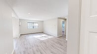 This 1-bedroom, 1-bathroom residence is laid out across a single floor, offering a clean and functional design with modern updates throughout. The open living area is spacious and filled with natural light streaming through multiple windows fitted with blinds. Light-toned luxury vinyl plank flooring runs throughout the main living spaces, complemented by neutral gray walls and recessed lighting that creates a bright, airy atmosphere. A sliding glass door in one of the living areas provides additional natural light and outdoor access. The two connected living areas offer flexible use of space, flowing seamlessly into one another. The kitchen is a standout feature, showcasing white shaker-style cabinetry, a light subway tile backsplash, dark countertops, and a full suite of stainless steel appliances including a refrigerator, range, and dishwasher. Light wood-look flooring continues into the kitchen for a cohesive look. The generously sized bedroom features plush carpeting, two windows for ample natural light, and a wall-mounted A/C unit. The bathroom is finished with large-format white tile surrounding a full soaking tub and shower combination. A hallway connects the main living spaces, completing this well-organized and move-in-ready home.
