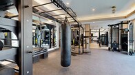 Located at 518 W 8th St in Dallas, TX, this contemporary fitness center offers a generously sized, single-floor layout designed to accommodate a full range of workout disciplines. The space is divided into two distinct zones that transition seamlessly from one to the next.

The first zone features light hardwood-style flooring, tall ceilings with sleek linear pendant lighting, and large windows that invite abundant natural light and views of the surrounding neighborhood. This area is outfitted with Matrix cable machines, multi-functional strength stations, and adjustable benches, providing a clean and modern environment for resistance training.

The second zone transitions to durable rubber flooring and is anchored by a tray ceiling with recessed lighting and ceiling fans, creating a comfortable atmosphere for high-intensity training. Floor-to-ceiling windows line one wall, flooding the space with daylight. This area houses a TRX suspension training rig, a heavy punching bag, additional cable and strength machines, and a full row of cardio equipment including treadmills, ellipticals, and stationary bikes. Full-length mirrors amplify the sense of openness throughout. A water fountain and additional amenities are accessible from within the space, rounding out this well-appointed fitness facility.